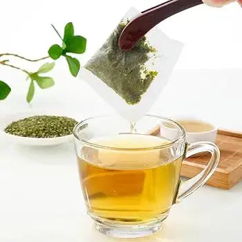 Person using a spoon to immerse an herbal tea bag in a clear glass cup of organic soursop tea.